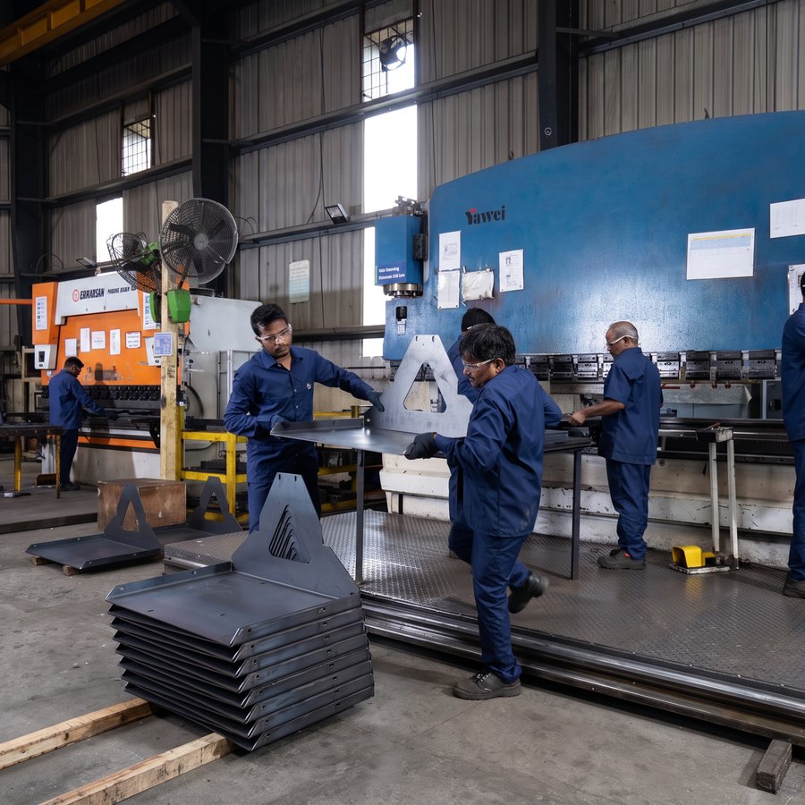 The press-brake bay in use, formed panels stacked in the foreground and operators working the machine