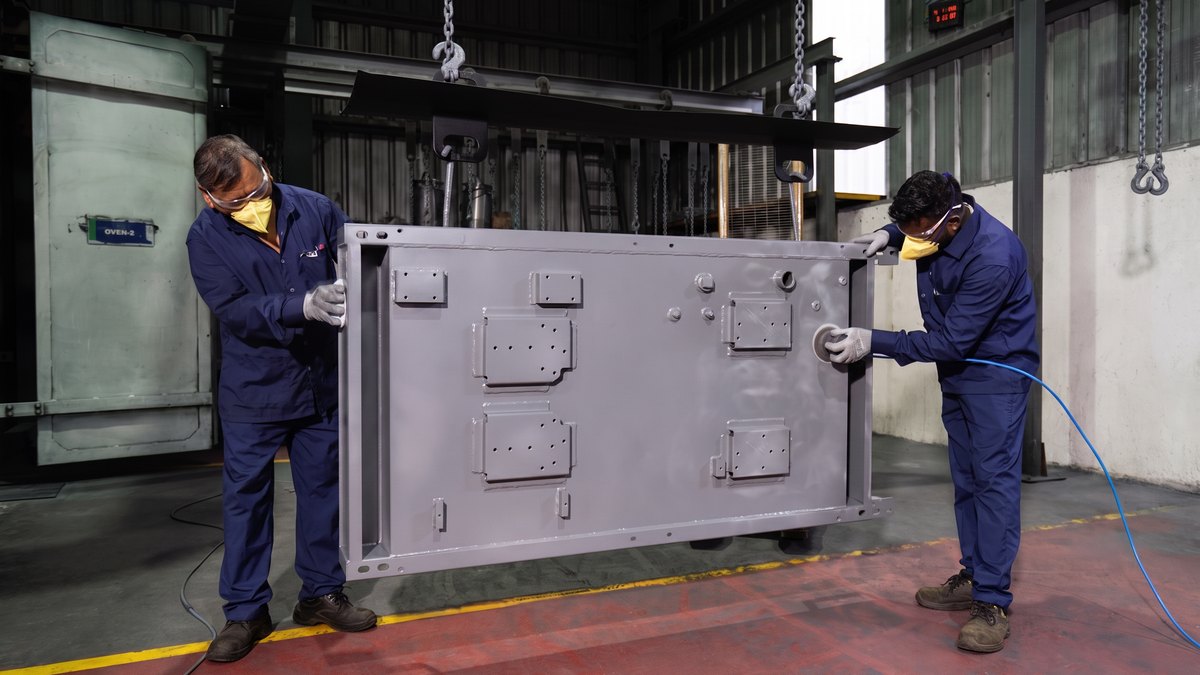 Two operators in respirators finishing a large fabricated panel in the coating bay